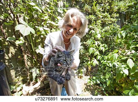 Senior woman cuddling cat while sitting in garden View Large Photo Image Stock Image - Senior woman cuddling cat while sitting in garden. Fotosearch
