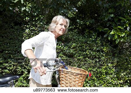 Senior woman looking away while standing with bicycle at backyard View Large Photo Image Stock Image - Senior woman looking away while standing with bicycle at backyard. Fotosearch