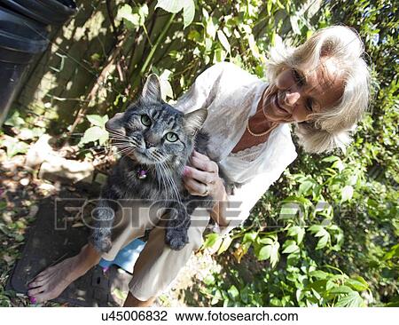 Senior woman stroking cat while sitting in garden View Large Photo Image Stock Image - Senior woman stroking cat while sitting in garden. Fotosearch