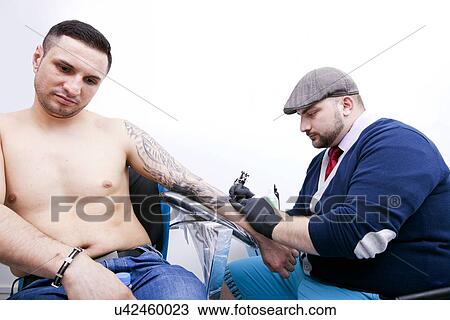 Shirtless young man getting tattoo on arm in parlor View Large Photo Image Stock Image - Shirtless young man getting tattoo on arm in parlor. Fotosearch
