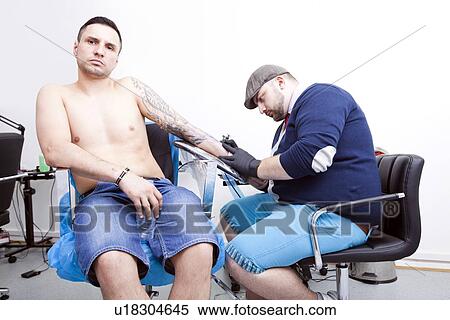 Shirtless young man getting tattooed on arm from artist in tattoo shop View Large Photo Image Stock Photography - Shirtless young man getting tattooed on arm from artist in tattoo shop. Fotosearch