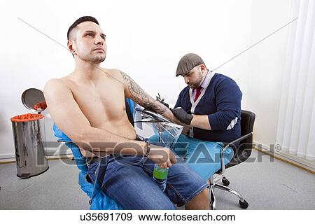 Shirtless young man getting tattooed from artist in tattoo shop View Large Photo Image Stock Photo - Shirtless young man getting tattooed from artist in tattoo shop. Fotosearch