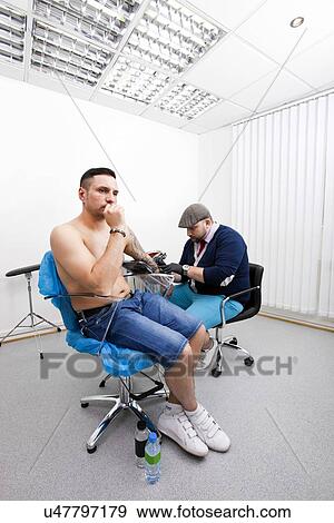 Shirtless young man getting tattooed from artist in parlor View Large Photo Image Stock Photo - Shirtless young man getting tattooed from artist in parlor. Fotosearch