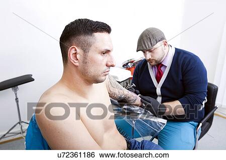 Shirtless young man getting tattooed from artist in tattoo shop View Large Photo Image Stock Photograph - Shirtless young man getting tattooed from artist in tattoo shop. Fotosearch