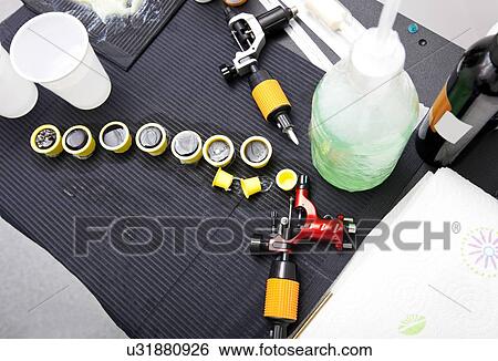 Stock Photograph - Tattoo gun, caps and ink bottle on table in shop. Fotosearch