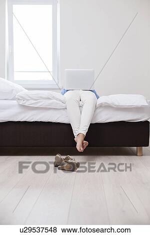 Stock Photo - Woman using laptop on her bed. Fotosearch