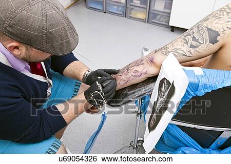 Young artist tattooing man's arm in tattoo parlor View Large Photo Image Stock Photograph - Young artist tattooing man's arm in tattoo parlor. Fotosearch