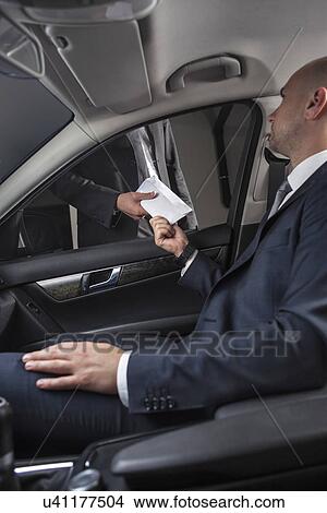 Young businessmen giving and receiving envelop through car window View Large Photo Image Picture - Young businessmen giving and receiving envelop through car window. Fotosearch