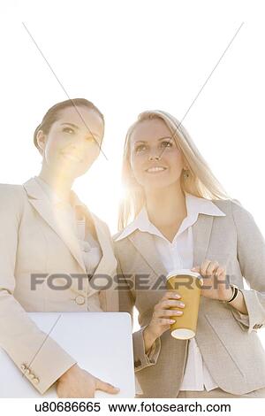 Young businesswomen with disposable cup and laptop looking away against sky View Large Photo Image Stock Photography - Young businesswomen with disposable cup and laptop looking away against sky. Fotosearch