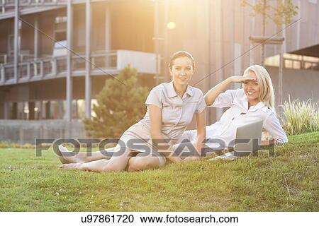 Stock Image - Young businesswomen with laptop relaxing on office lawn. Fotosearch