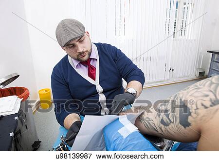 Young tattoo artist tattooing man's arm in studio View Large Photo Image Stock Photo - Young tattoo artist tattooing man's arm in studio. Fotosearch