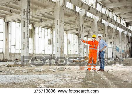 Stock Photograph - Full length of construction workers discussing at construction site. Fotosearch