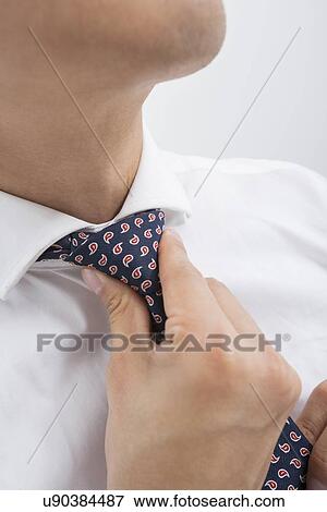 Stock Photo - Midsection of mid adult Asian businessman adjusting tie. Fotosearch