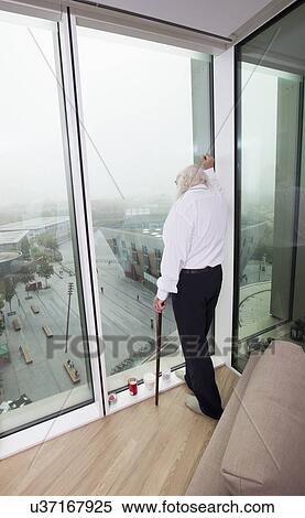 Thoughtful senior man looking through window View Large Photo Image Stock Photography - Thoughtful senior man looking through window. Fotosearch