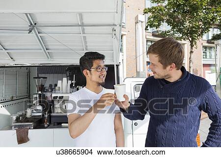 Picture - Vendor giving disposable coffee cup to customer against mobile shop. Fotosearch
