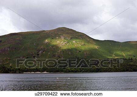 Stock Image - View of sea against mountain against cloudy sky. Fotosearch