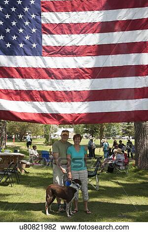Stock Image - Husband, wife and dog under US Flag in Ridgway, Colorado Town Park. Fotosearch