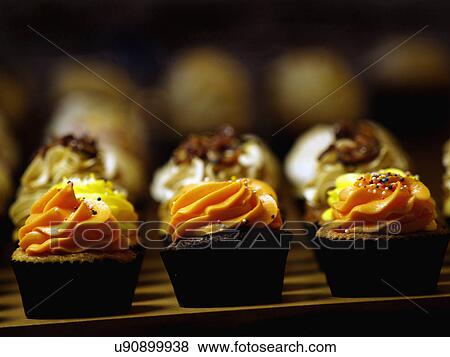 Stock Photo - Row Of Assorted Cupcakes With Orange Icing. Fotosearch