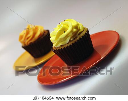 Two Iced Lemon And Orange Cupcakes On Red Plate View Large Photo Image Picture - Two Iced Lemon And Orange Cupcakes On Red Plate. Fotosearch