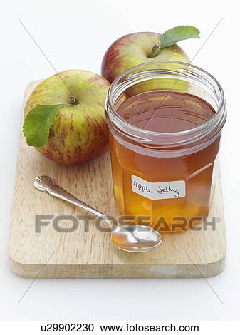 Stock Image - A glass jar of apple jelly with whole apples behind. Fotosearch