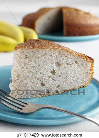 Stock Photo - A slice of banana cake with a whole cake and fruit behind. Fotosearch