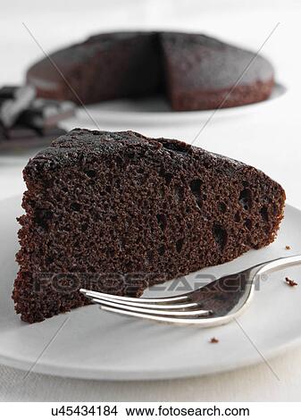 A slice of chocolate cake with a whole cake and chocolate pieces behind View Large Photo Image Picture - A slice of chocolate cake with a whole cake and chocolate pieces behind. Fotosearch