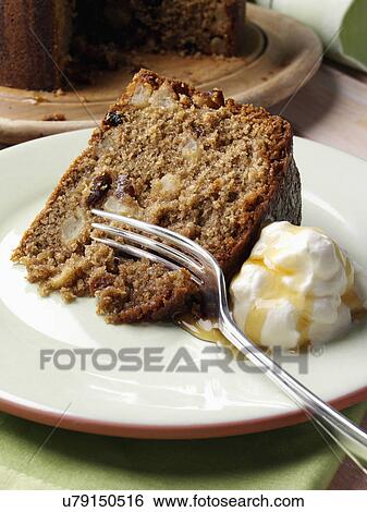 Stock Photograph - A whole Somerset apple cake with a slice on a plate in front with cream and honey. Fotosearch