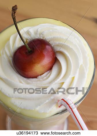 Stock Image - Banana milkshake with whipped cream topping and a ripe cherry on top. Fotosearch