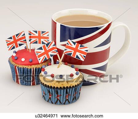 Stock Image - British Themed Celebration Cupcakes, White And Red Iced Sponge Fairy Or Cup Cake, Topped With Red, White And Blue Sprinkles, Small Union Jack Flags, Union Jack Mug Of Tea, All On White Background. Fotosearch
