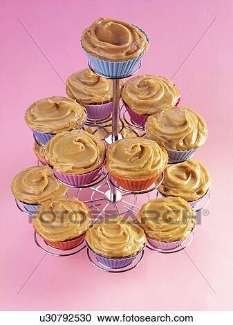 Stock Image - Cake Stand Full Of Caramel Toffee Cupcakes With Butter Cream Topping, Pink Background. Fotosearch