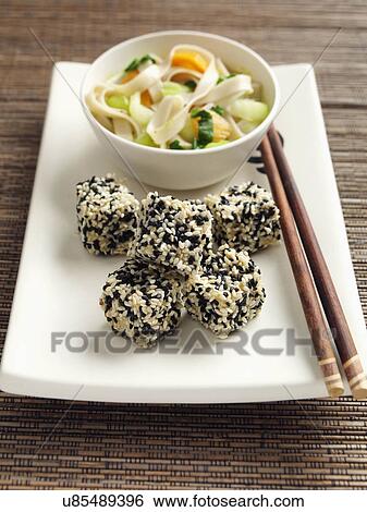 Stock Photograph - Deep fried tofu coated in black and white sesame seeds rice noodles stir fried vegetables carrots scallions sugar snaps Japanese main meals. Fotosearch