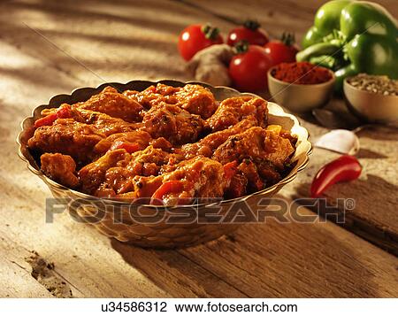 Stock Image - Dish Of Chicken Balti Curry With Sunlit Tabletop, Tomatoes And Green Peper. Fotosearch