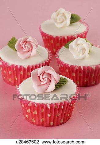 Stock Image - Four Perfect White Iced Cupcakes In Pink Polka Dot Cake Cases Decorated With Single Sugar Craft Rose, On Pink Tabletop. Fotosearch