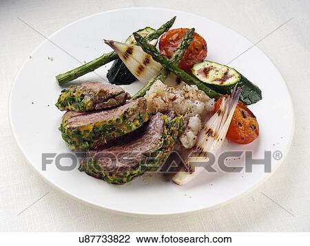 Stock Image - Lamb rump with a herb and mustard crust asparagus shallots courgettes and tomatoes. Fotosearch