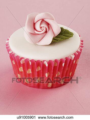 Stock Image - One Perfect White Iced Cupcake In Pink Polka Dot Cake Case Decorated With Single Pink Sugar Craft Rose, On Pink Tabletop. Fotosearch
