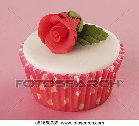 Stock Photo - One Perfect White Iced Cupcake In Pink Polka Dot Cake Case Decorated With Single Red Sugar Craft Rose, On Pink Tabletop. Fotosearch