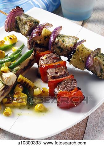 Stock Image - Pork and pineapple and chilli beef kebabs with corn and palm heart salad. Fotosearch
