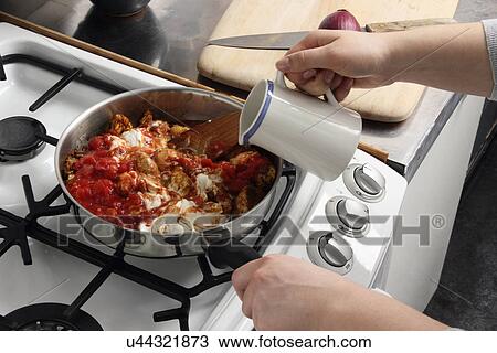 Stock Image - Pouring into a simmering pan of chicken rogan josh. Fotosearch