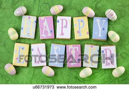 Stock Image - Row Of Wrapped Candy Or Chocolate Bars With Letters Spelling Greeting, Happy Easter, On Green Background With Small Easter Eggs. Fotosearch