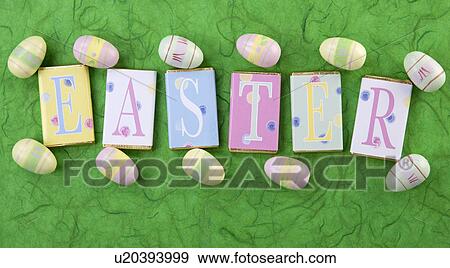 Stock Photo - Row Of Wrapped Candy Or Chocolate Bars With Letters Spelling Greeting, Easter, On Green Background With Small Easter Eggs. Fotosearch