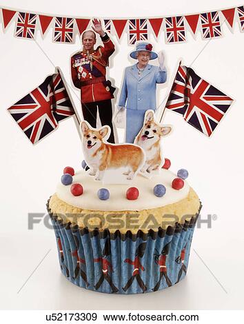 Stock Photo - Royal Themed British Celebration Cupcake, White Iced Sponge Fairy Or Cup Cake, Topped With Red And Blue Sprinkles Two Small Union Jack Flags, A Waving Queen Elizabeth, And Prince Philip And Two Corgi Dogs. On White Background With Union Jack Bunting. Fotosearch
