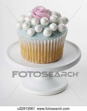 Stock Image - Single Pastel Blue Cupcake With Single Rose And Large Pearl Decorations, On Small White Cake Stand. Fotosearch