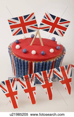 Stock Photography - Themed British Celebration Cupcake, Red Iced Sponge Fairy Cake, Topped With White And Blue Sprinkles And Small Union Jack Flags, On White With Union Jack Bunting. Fotosearch