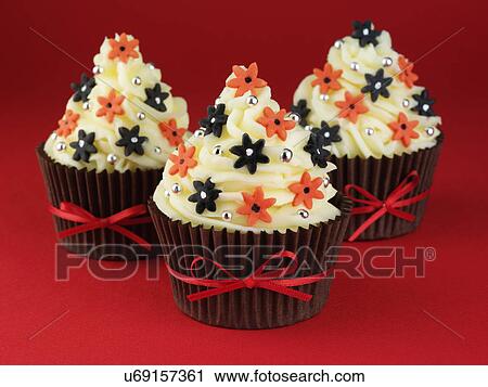Stock Image - Three Buttercream Topped Cupcakes With Red And Black Flower Decorations, Brown Cake Cases Tied With Red Ribbon. Fotosearch