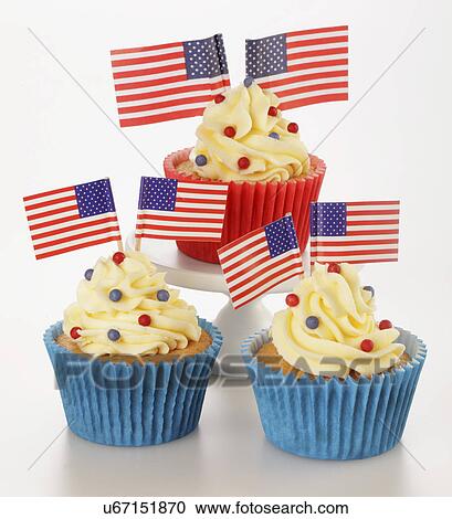 Stock Image - Three Cupcakes In Red And Blue Cases Decorated With Buttercream Fondant And Topped With Small American Flags And Sprinkles, White Tabletop. Fotosearch