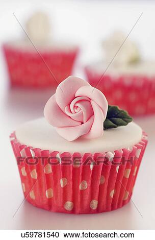 Stock Image - Three Perfect White Iced Cupcakes In Pink Polka Dot Cake Cases Decorated With Single Sugar Craft Roses, On White Tabletop. Fotosearch