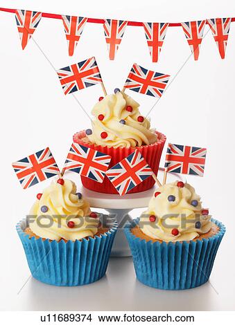 Picture - Three Themed British Celebration Cupcakes, Red And Blue Cake Case Filled With Sponge Cake, Topped With Buttercream Red And Blue Sprinkles And Small Union Jack Flags, On White With Union Jack Bunting. Fotosearch