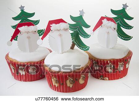 Stock Photograph - Three White Iced Sponge Cupcakes In Paper Cases Topped With Father Christmas, Christmas Tree, White Background. Fotosearch