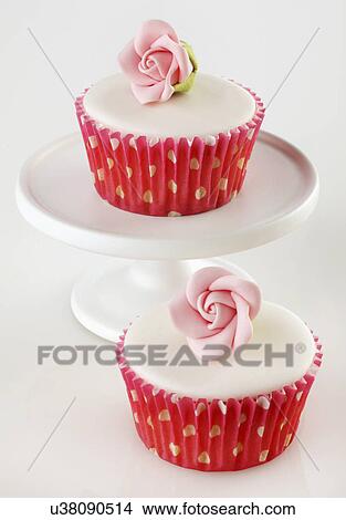Picture - Two Perfect White Iced Cupcakes In Pink Polka Dot Cake Cases Decorated With Single Sugar Craft Rose, One Cake On White Cake Stand, Pink Tabletop. Fotosearch