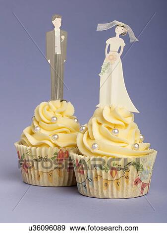 Two Wedding Cupcakes With Piped Buttercream Topping Decorated With Pearls. Bride Figurine On One Cake And Groom On Other. Purple/Blue Background View Large Photo Image Stock Photo - Two Wedding Cupcakes With Piped Buttercream Topping Decorated With Pearls. Bride Figurine On One Cake And Groom On Other. Purple/Blue Background. Fotosearch